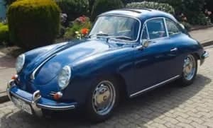 Dunkelblauer Porsche 356 Oldtimer vor einer Hecke.