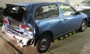 Blauer Kleinwagen mit eingedrücktem Heck und Seitenschaden.